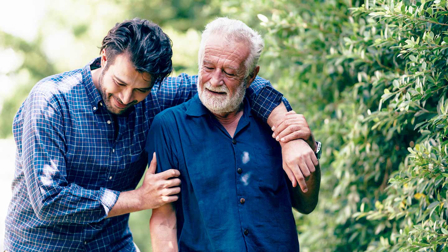 Two men hugging an older man in a park.