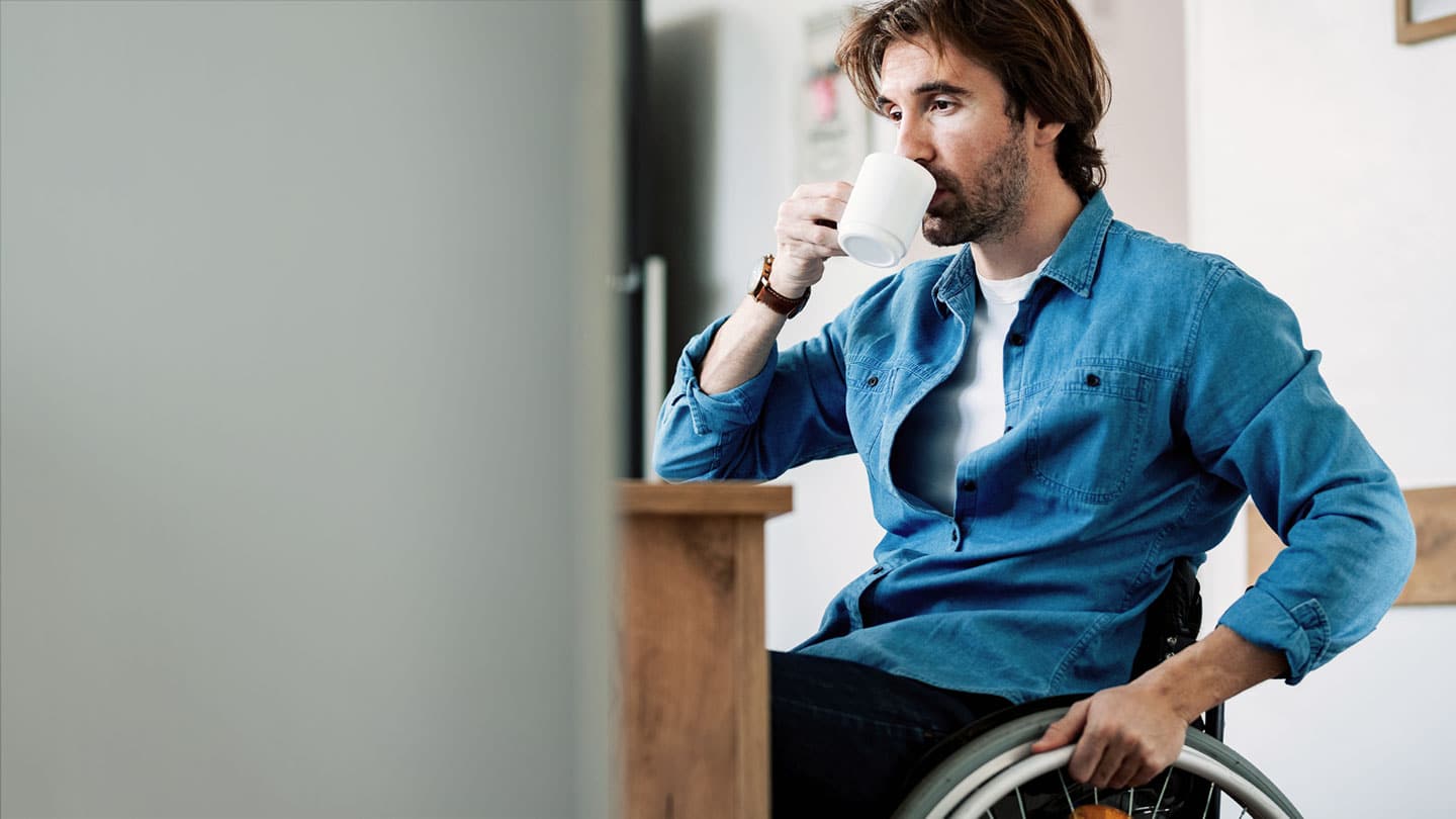 A man in a wheelchair drinking a cup of coffee.