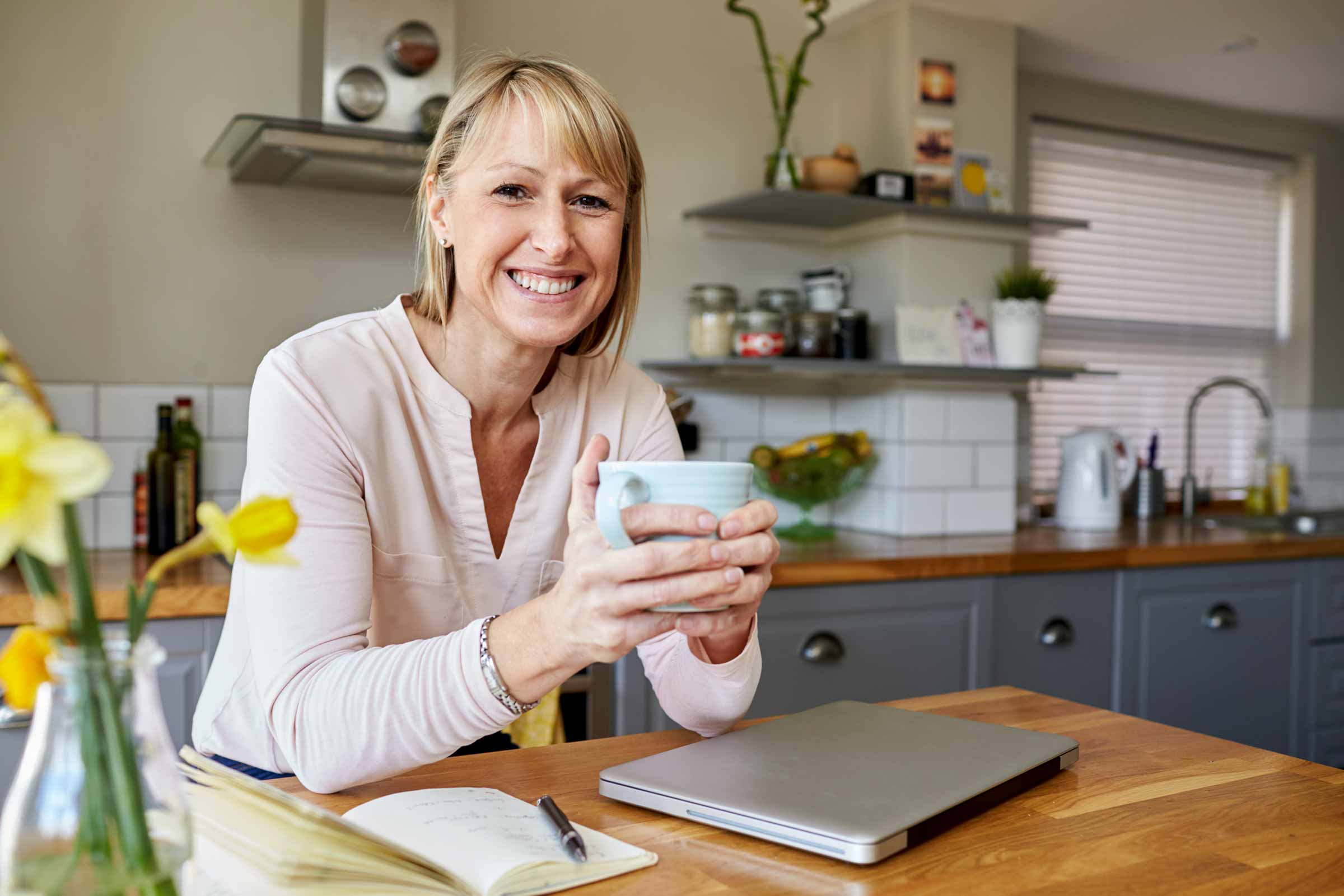 A woman holding a cup of coffee in front of a laptop.
