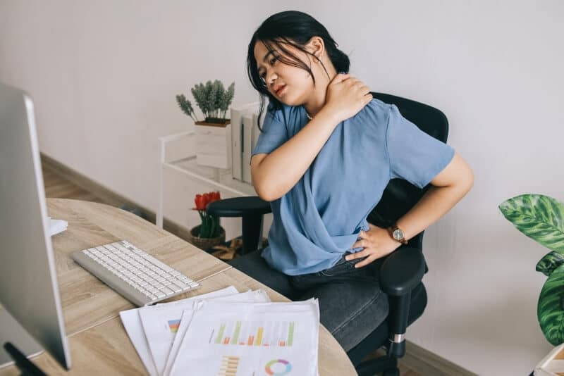 A woman is sitting at her desk with a pain in her neck.